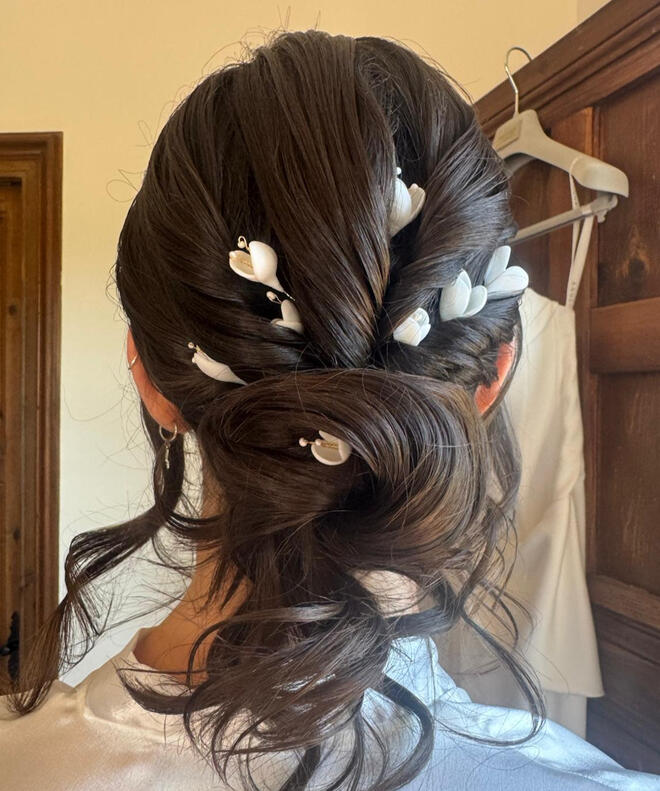 Novia luciendo un recogido desestructurado bajo con horquillas artesanales porcelana fría blanca en forma de tulipanes decorando el peinado. Creadas a mano, pétalo a pétalo por Pajarita Presumida. Son ligeras, sostenibles, versátiles, únicas y personalizab