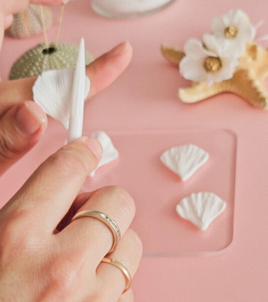 Artesana creando pétalos de porcelana fría a mano, proceso artesanal tocados de boda, horquillas artesanales personalizadas sobre caparazón erizo marino, complementos boda únicos flores artesanales.