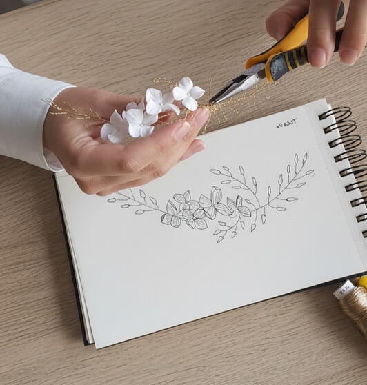 Artesana creando tocado de boda personalizado sobre boceto dibujado a mano, alambre dorado y flores de porcelana fría, diseño único tocados nupciales personalizados artesanales exclusivos y sostenibles.