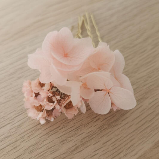 Horquillas de hortensias preservadas en tonos rosas claros, delicadeza artesanal. Horquillas artesanales de hortensia natural preservada y glíxia en tonos rosas claros, dispuestas sobre mesa de madera. Complemento floral hecho a mano en Mallorca, ideal para comunión, novias o invitadas