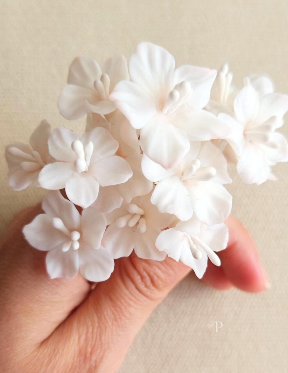 Mano sosteniendo horquillas artesanales de novia con flores silvestres blancas y sutiles pinceladas rosas, hechas a mano en porcelana fría por Pajarita Presumida.