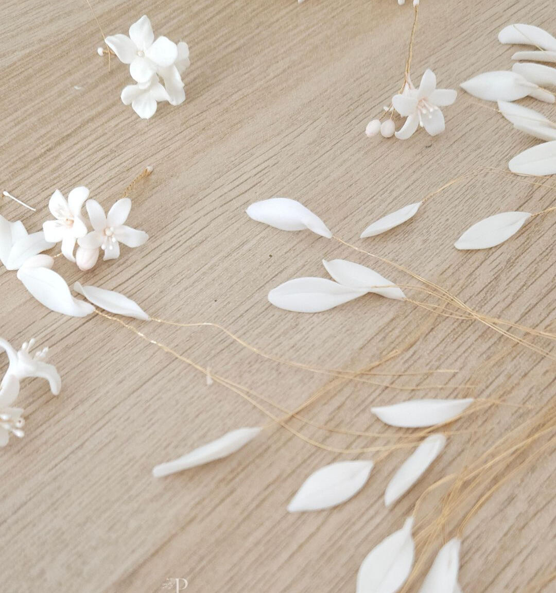 Flores de naranjo y hojas de olivo recién modeladas en porcelana fría blanca sobre la mesa de trabajo, inicio del proceso artesanal que dará lugar a horquillas y tocados de novia hechos a mano, pensados para mujeres que apuestan por la artesanía, el lujo c