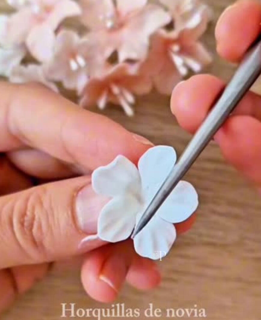 Mano modelando una flor de porcelana fría blanca con herramienta de modelado, dando forma pétalo a pétalo en un proceso artesanal lento y preciso. Cada flor se crea a mano, sin moldes, para dar vida a piezas únicas.